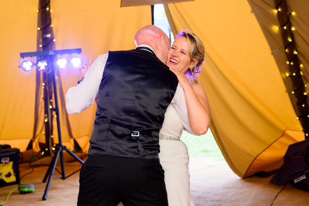 Fun bride and groom laughing whilst dancing together inside wedding tipi