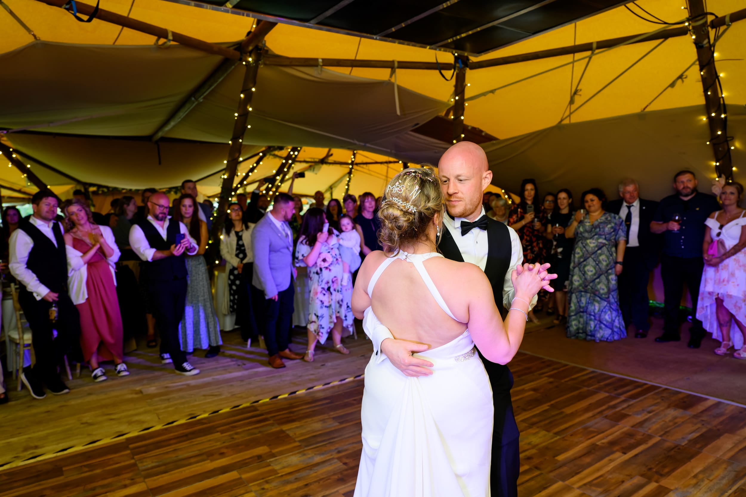 Bride and groom surrounded by guests during their first dance inside wedding tipi