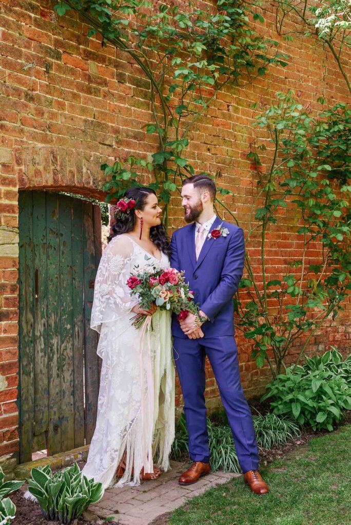 Bohemian bride and groom in front of rustic green garden door & brick wall