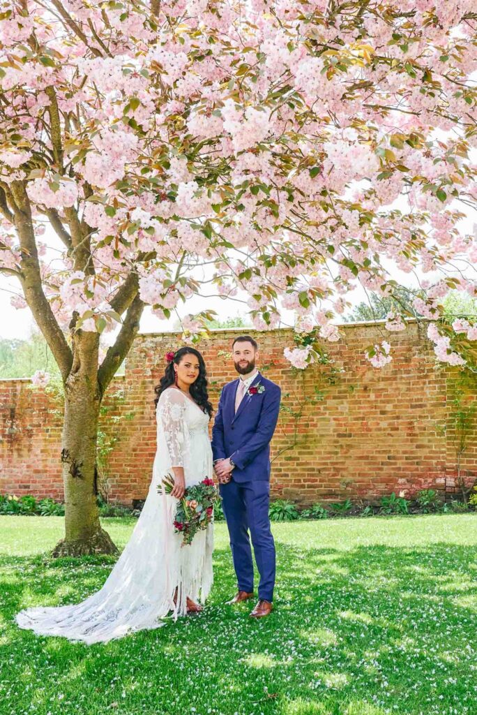 bohemian couple stood under cherry blossom tree in front of brick wall