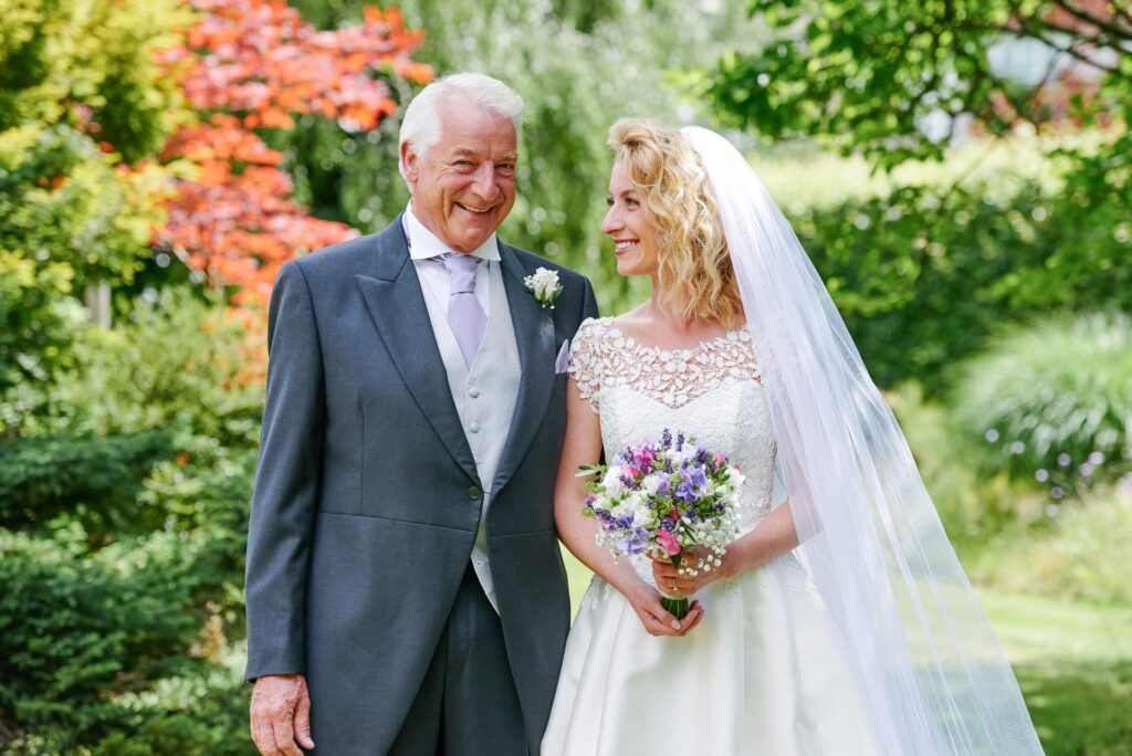 bride  with her dad smiling in front of colourful green plants on sunny wedding day