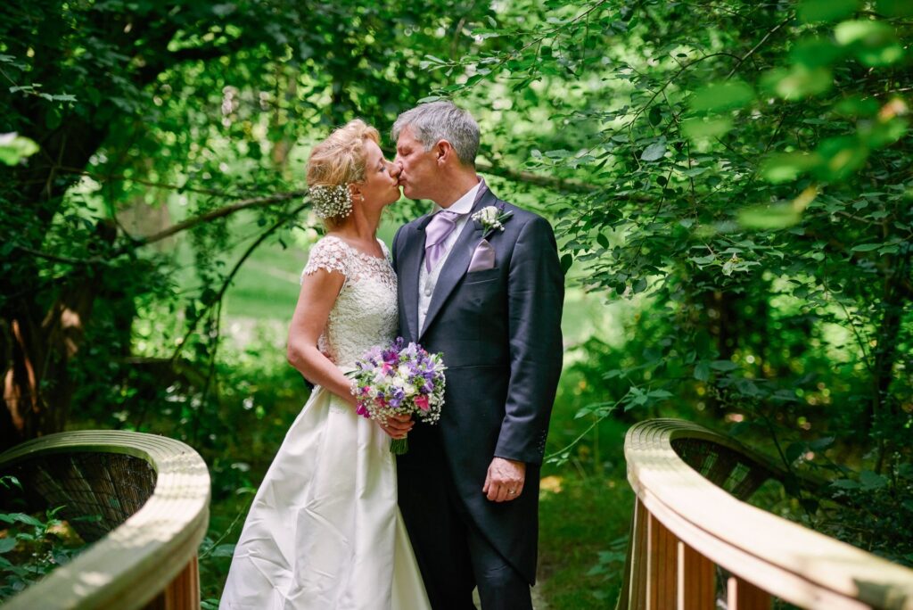 bride and groom kissing on a bridge with green foliage behind