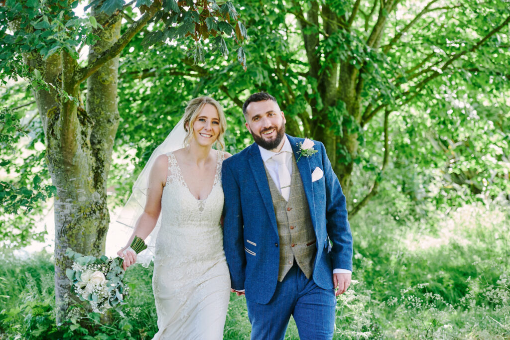 Bride and groom walking through green foliage during their wedding photoshoot