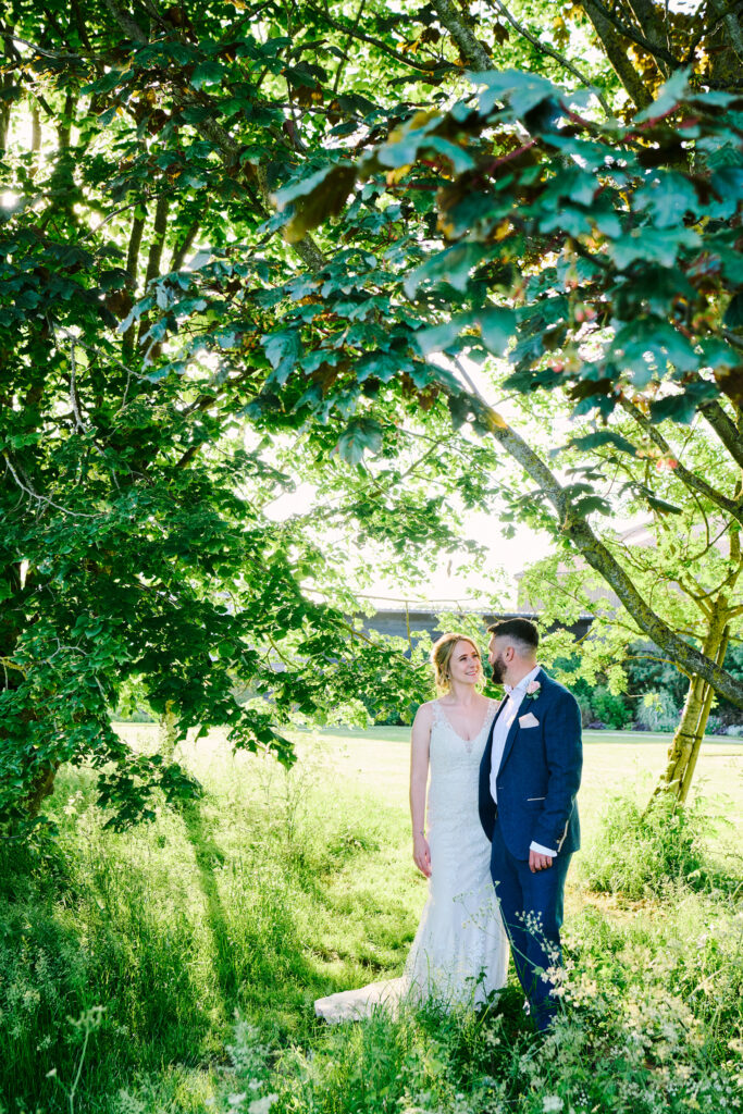 bride and groom stood together in sunlight surrounded by trees