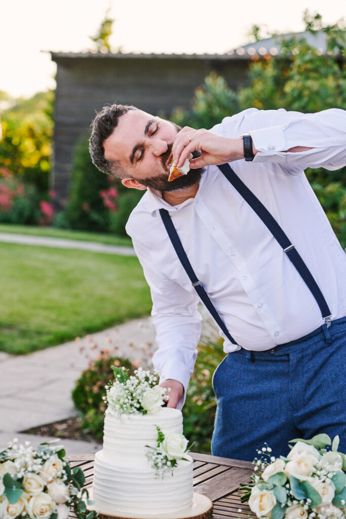 groom eating some wedding cake whilst stood outside during sunny evening