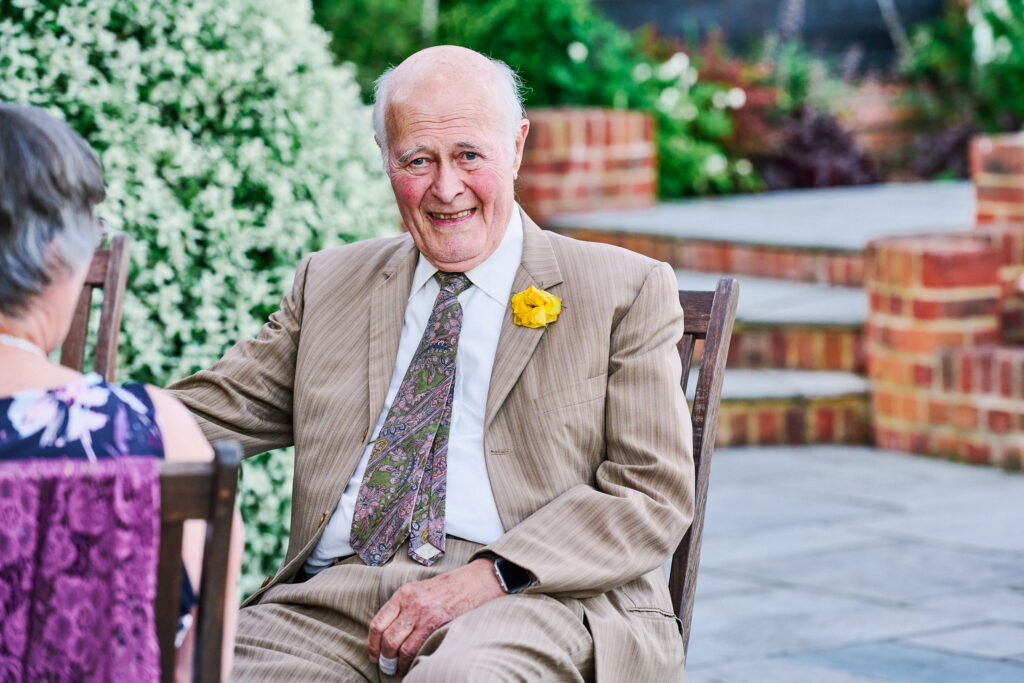 old man wedding guest smiling whilst sat outside