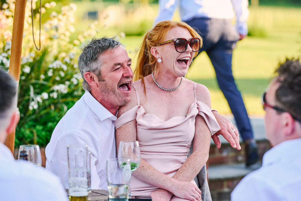 wedding guests laughing whilst sat in the sun at stokes farm barn