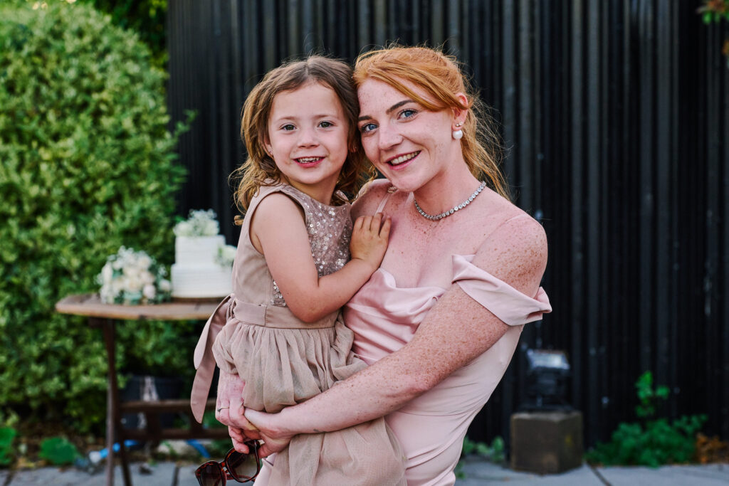 Bridesmaid holding her daughter whilst smiling and stood outside