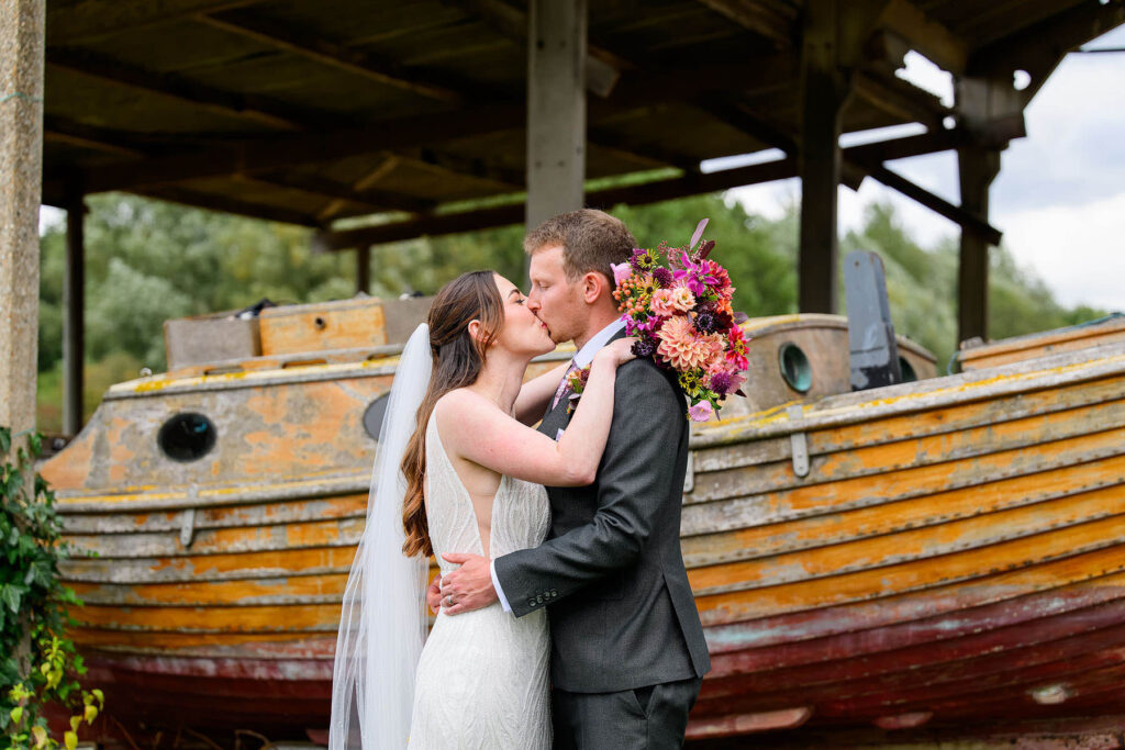 bride & groom kissing in front of boat at Willow Marsh Farm