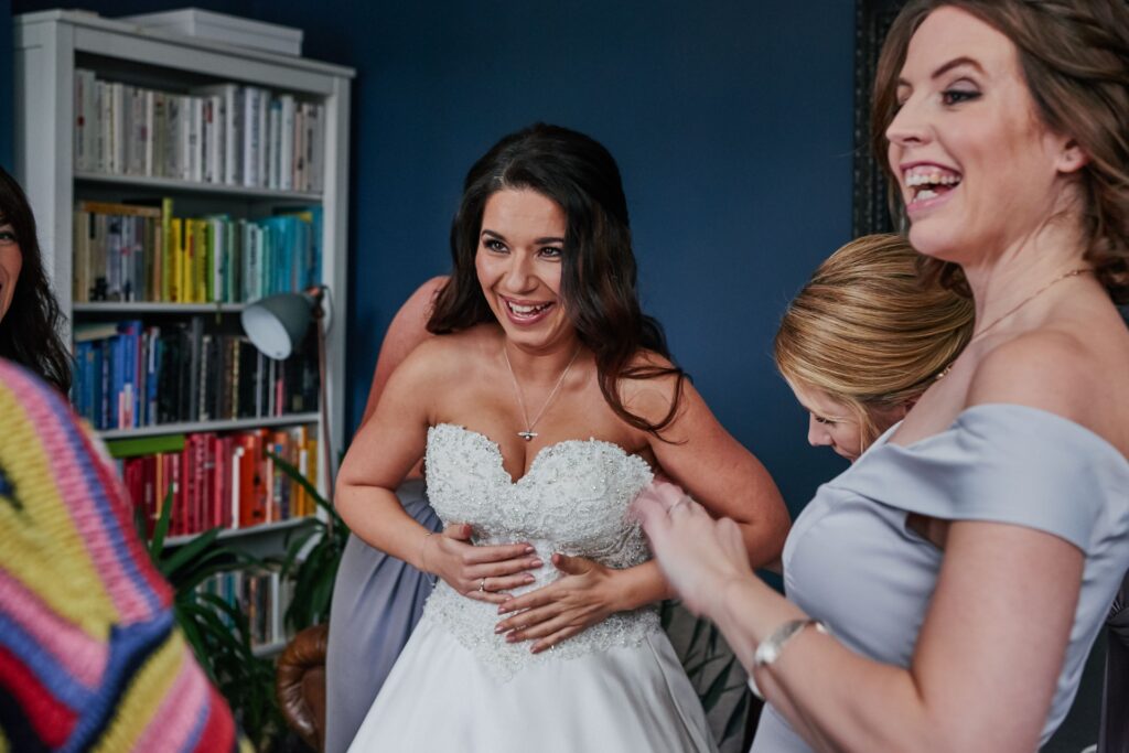 Bride laughing whilst putting on her wedding dress