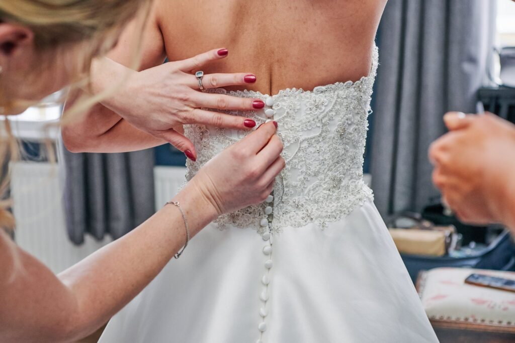 Bride having her dress buttoned up during bridal prep