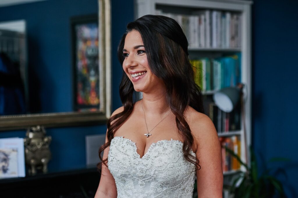 Bride smiling whilst putting on her wedding dress
